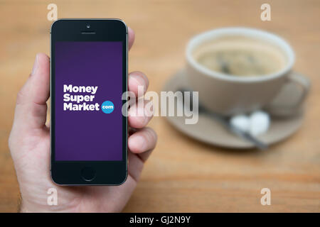 Un homme se penche sur son iPhone qui affiche le logo du supermarché de l'argent, alors qu'assis avec une tasse de café (usage éditorial uniquement). Banque D'Images