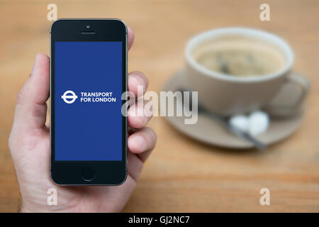 Un homme se penche sur son iPhone qui affiche le logo Transport for London, en restant assis avec une tasse de café (usage éditorial uniquement). Banque D'Images