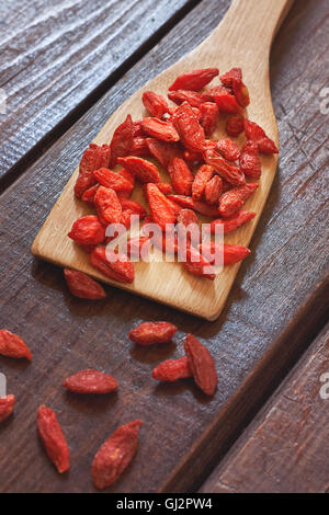 Baies de goji séchées en cuillère en bois sur fond de bois. Banque D'Images