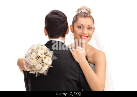 Happy young bride hugging groom et tenant un bouquet dans sa main isolé sur fond blanc Banque D'Images