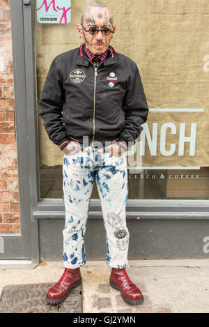 Un punk tatouée en jeans et rouge Doc Martens aux portes d'une boutique sur la rue principale. Banque D'Images