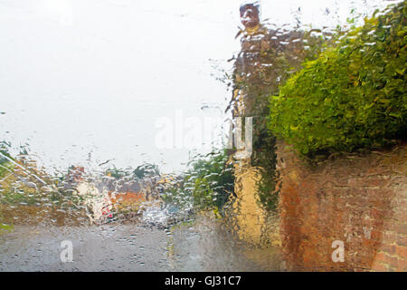 Route de village, mur et haie photographié par une pluie pare-brise Banque D'Images