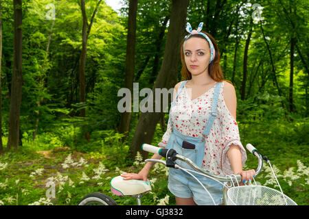 Femme portant des quartiers et d'une salopette en jean ample chemisier avec son vélo dans un parc Banque D'Images