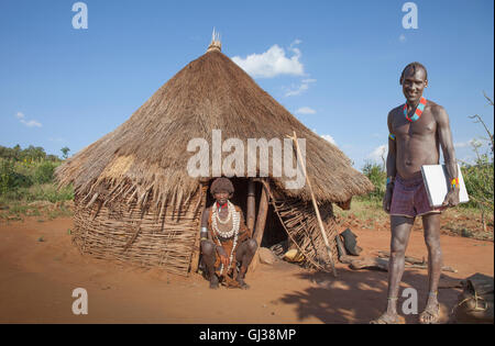 L'homme de la tribu Karo avec ordinateur portable, tandis que sa femme dans une cabane est à regarder, vallée de l'Omo, Ethiopie Banque D'Images