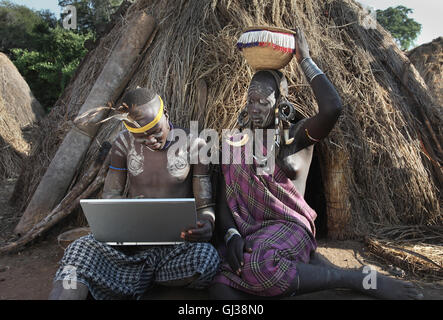 L'homme de la tribu Mursi avec ordinateur portable, assis à côté de sa femme, vallée de l'Omo, Ethiopie Banque D'Images