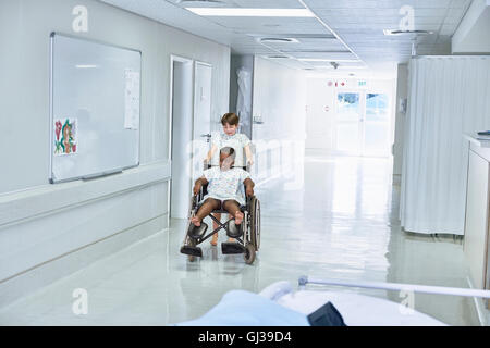 Les patients de sexe féminin ami garçon poussant en fauteuil roulant à l'hôpital de pédiatrie Banque D'Images