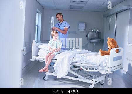 Garçon assis sur le lit du patient à regarder ours à l'hôpital de pédiatrie Banque D'Images