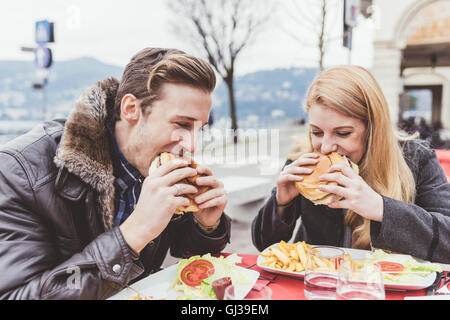 Jeune couple eating burgers at sidewalk cafe, Le Lac de Côme, Italie Banque D'Images