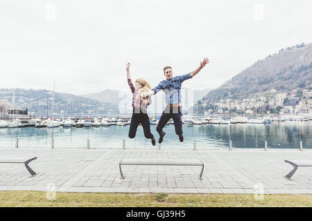 Jeune couple sur le bord de jumping mid air, Lac de Côme, Italie Banque D'Images