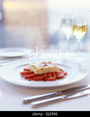 Filet de poisson garni de fromage fondu sur un lit de tomates assaisonnées d'huile d'olive et vinaigre balsamique Banque D'Images