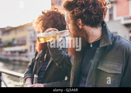 Jeune homme aux cheveux rouges jumeaux hipster et barbes de boire une bière sur canal mer Banque D'Images