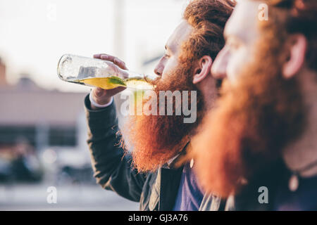 Profil de jeune homme hipster twins avec les cheveux rouges et barbes de boire la bière en bouteille Banque D'Images