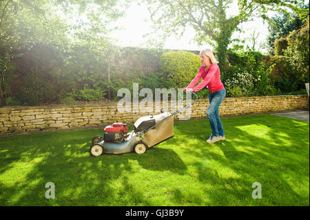 Femme mature de la tonte de pelouse jardin ensoleillée avec tondeuse Banque D'Images