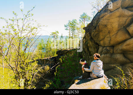 Female hiker et son bulldog assis sur la roche de la montagne avec vue sur la forêt, la Russie Banque D'Images