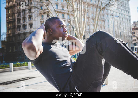 Jeune homme exerçant à l'extérieur, faire des sit-ups Banque D'Images