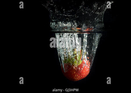 Strawberry tombe profondément sous l'eau avec une éclaboussure. Tout est sur l'arrière-plan noir. Banque D'Images