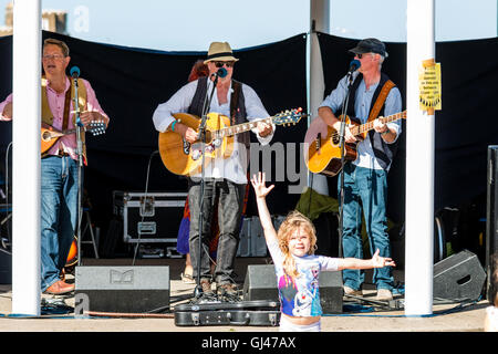 Festival de la semaine folklorique de Broadstairs. Trois morceau senior male folk ensemble jouant dans le kiosque avec un petit enfant, Girl standing in front, voler la vedette en donnant des directives. Banque D'Images