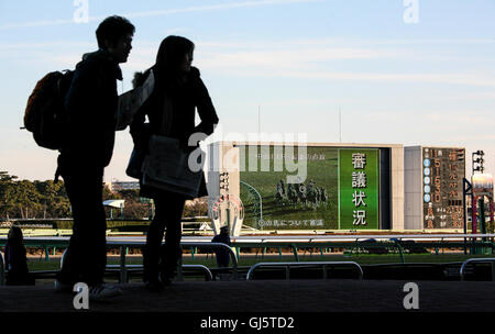 Jeune couple de quitter le stand. Beaucoup de quitter après l'événement principal de la journée, la 11e course. Le grand écran montrant une répétition de ra Banque D'Images