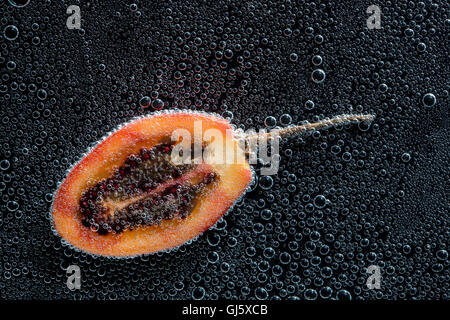 Tamarillo réduit de moitié des fruits dans de l'eau minérale, une série de photos. Close-up de l'eau gazéifiée sur fond noir Banque D'Images