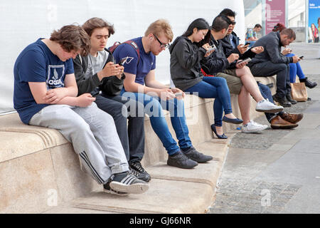 Les jeunes se sont assis tous sur des téléphones portables accédant aux réseaux numériques, aux communications d'interaction des médias sociaux modernes à Liverpool, au Royaume-Uni Banque D'Images