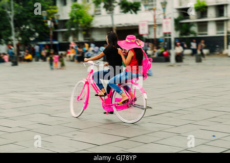 Deux jeunes filles en rose hat de rouler à vélo en ville de Jakarta. Les personnes actives. À l'extérieur Banque D'Images