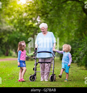 Happy senior dame avec une marchette tenant la main de petit garçon et fille. Grand-mère grand avec les enfants bénéficient à pied en été park Banque D'Images