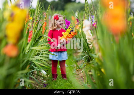 Little girl holding glaïeul fleurs''. Préparation de l'enfant des fleurs fraîches dans le jardin. Jardinage Enfants en automne Banque D'Images