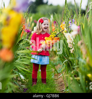 Little girl holding glaïeul fleurs''. Préparation de l'enfant des fleurs fraîches dans le jardin. Jardinage Enfants en automne Banque D'Images