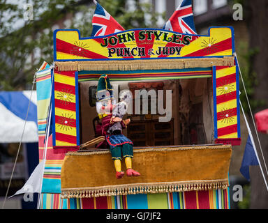 Version complète du corps de Mr Punch tenant le bébé dans ses bras devant un stand de marionnettes Punch and Judy Banque D'Images