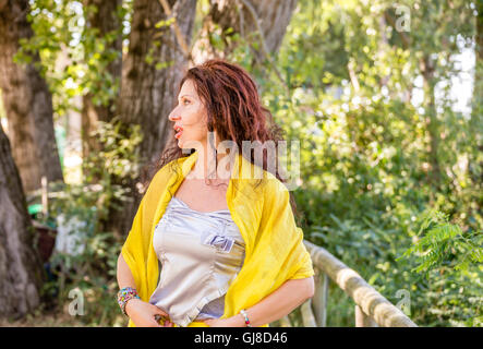 Vue de côté de l'élégant et glamour woman jupe jaune et argent et châle haut tout en parlant dans un parc verdoyant Banque D'Images