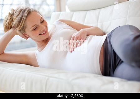 Parution du modèle. Pregnant woman lying on sofa de toucher son ventre. Banque D'Images