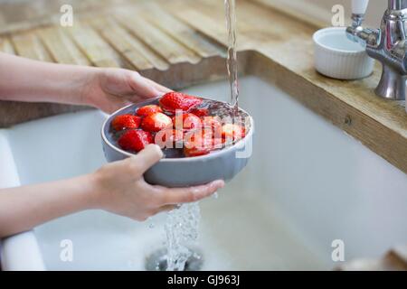 Parution de la propriété. Parution du modèle. Girl washing fraises fraîches dans l'évier. Banque D'Images