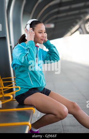 Parution du modèle. Jeune femme assise sur un quai de gare portant des écouteurs. Banque D'Images