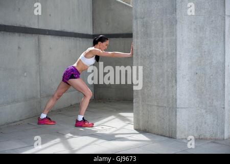 Parution du modèle. Young woman stretching contre mur. Banque D'Images