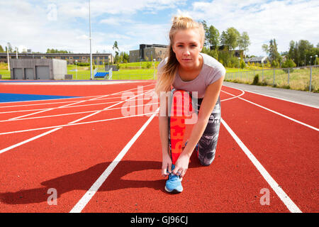 Athletic coureuse de lier ses lacets sur une piste de course Banque D'Images