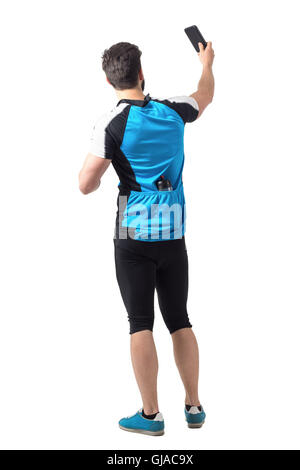 Vue arrière du cycliste à jersey shirt avec de l'eau bouteille dans les poches arrière de prendre une photographie. La longueur du corps complet isolé portrait Banque D'Images