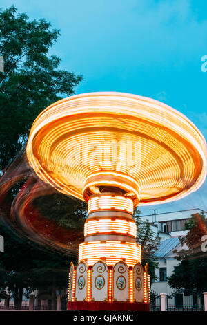 Effet de mouvement floue autour de éclairées Carrousel rotatif à grande vitesse Merry-Go-Round. Soir d'été en ville Amuseme Banque D'Images