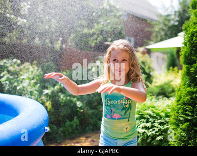 Bambin mignon fille jouant avec jardin arroseur. Piscine d'été de plaisir de l'eau dans la cour. Banque D'Images