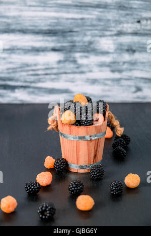 Framboises noires et jaunes dans un panier en bois gris sur fond de bois. Close up. Banque D'Images