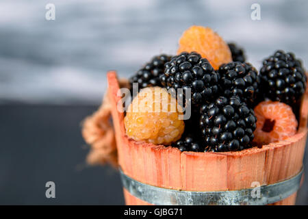 Framboises noires et jaunes dans un panier en bois gris sur fond de bois. Close up. Banque D'Images