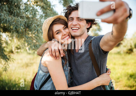 Young smiling couple heureux avec sacs à dos randonnée dans la forêt et faire selfies Banque D'Images