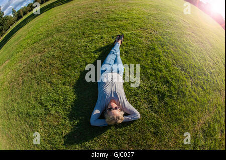 Une fille se trouve sur l'herbe dans un parc de Londres sous le soleil Banque D'Images