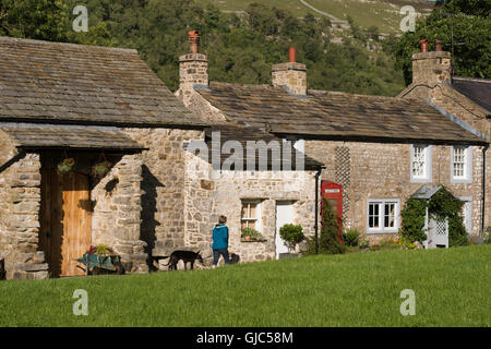 Lady dog walking, passe pittoresque, stone cottages à Arncliffe, un joli village, dans le Yorkshire Dales National Park, England. Banque D'Images