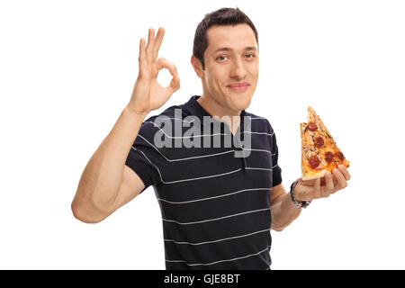 Jeune homme joyeux de manger une pointe de pizza et de faire un geste avec sa main ok isolé sur fond blanc Banque D'Images