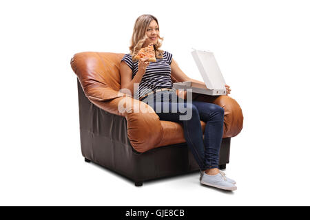 Jeune femme assise sur un fauteuil ayant une pointe de pizza et regarder la télévision isolé sur fond blanc Banque D'Images