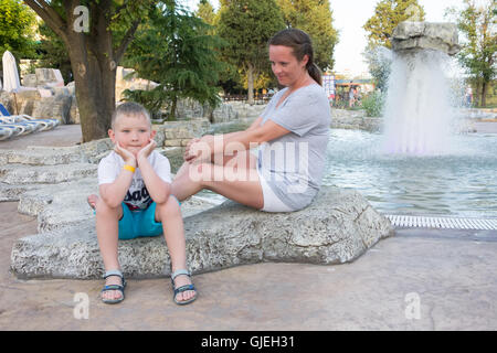 La mère et le fils assis sur un rocher et parler à la fontaine Banque D'Images