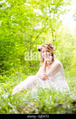 Mariée en robe de mariage avec couronne de fleurs, vert nature. Banque D'Images