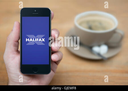 Un homme se penche sur son iPhone qui affiche le logo de la banque Halifax, alors qu'assis avec une tasse de café (usage éditorial uniquement). Banque D'Images