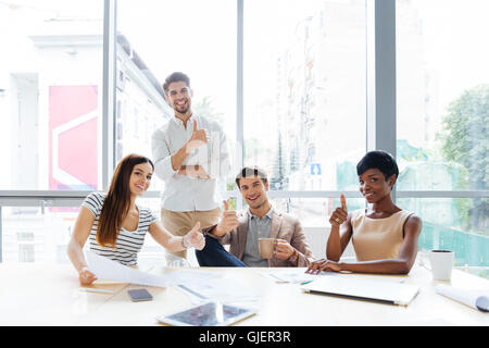 Succès joyeux groupe multiethnique de jeunes gens d'affaires showing Thumbs up in office Banque D'Images