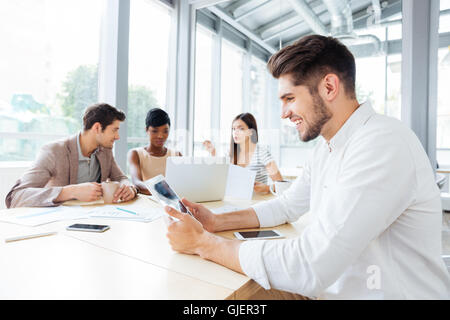 Happy handsome young businessman sitting and using tablet sur réunion d'affaires Banque D'Images